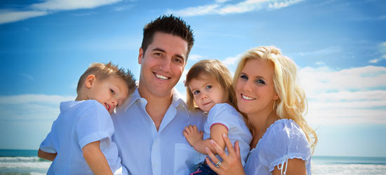 A smiling, happy family of four with two adults and two small children